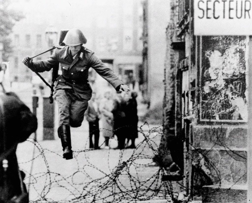 Conrad Schumann salta sopra il filo spinato raggiungendo la Germania Ovest. Berlino, 15 agosto 1961. Fotografia di Peter Leibing